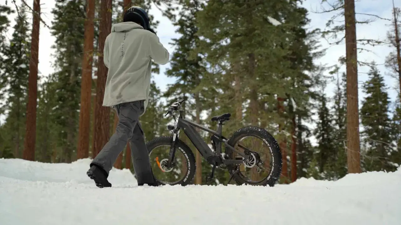 Man met helm loopt naast fatbike in de sneeuw. Goed om de fietsaccu bewaren in de winter op een droge plek.