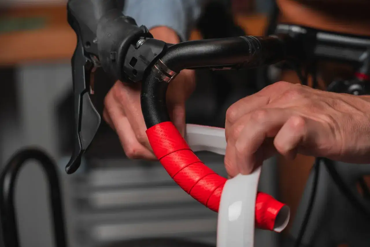 Handen zijn bezig met het stuurlint vervangen. Rode stuurlint wordt aangebracht op het zwarte fietsstuur.