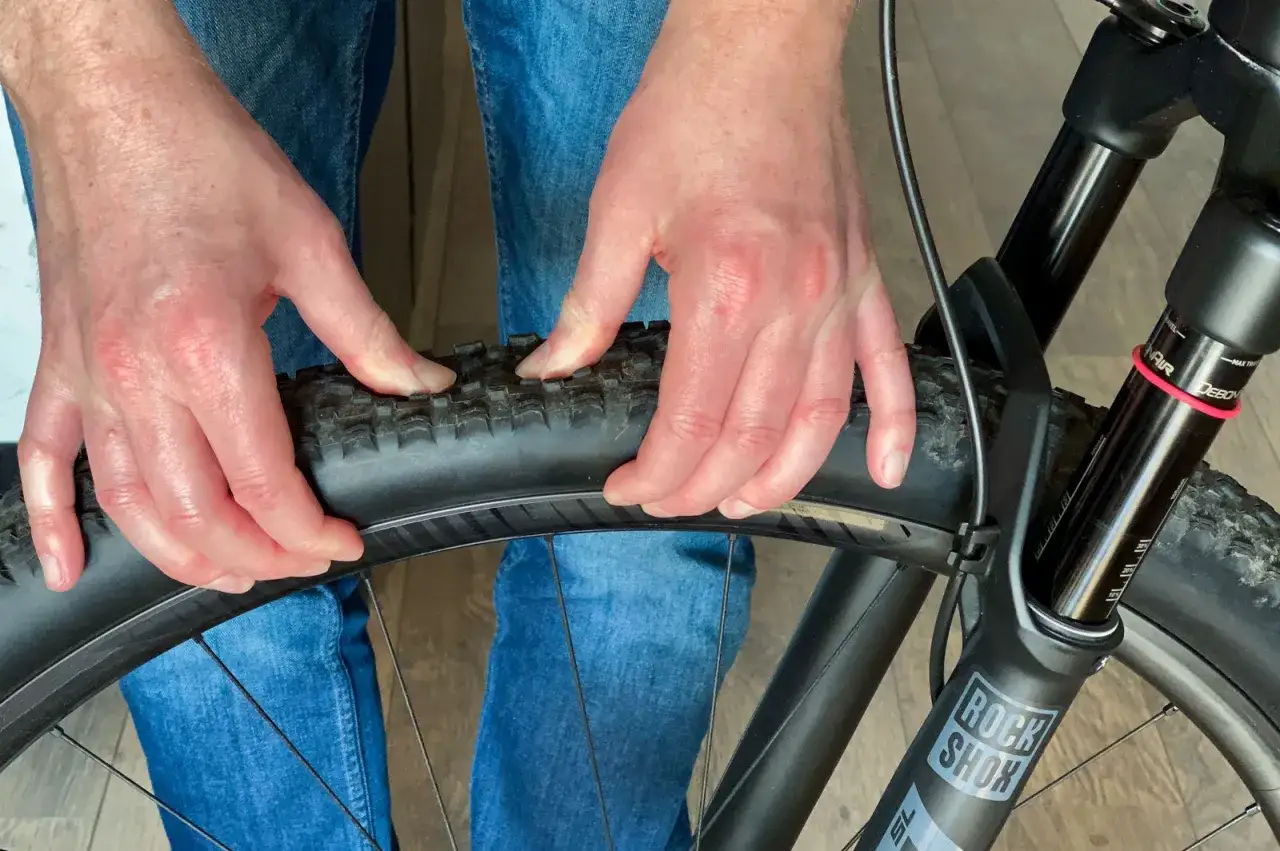 Handen controleren de bandenspanning van een mountainbike. De juiste bandenspanning is cruciaal voor een goede grip en comfort.