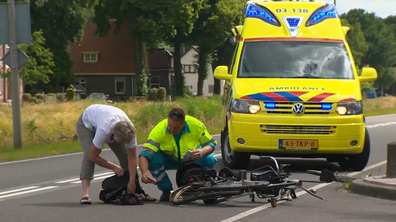 Een ambulance is ter plaatse na een ongeval. Een vrouw bukt zich bij een fiets, terwijl een ambulancebroeder toezicht houdt. Dit toont aan dat een fietser niet altijd beschermd is in het verkeer.