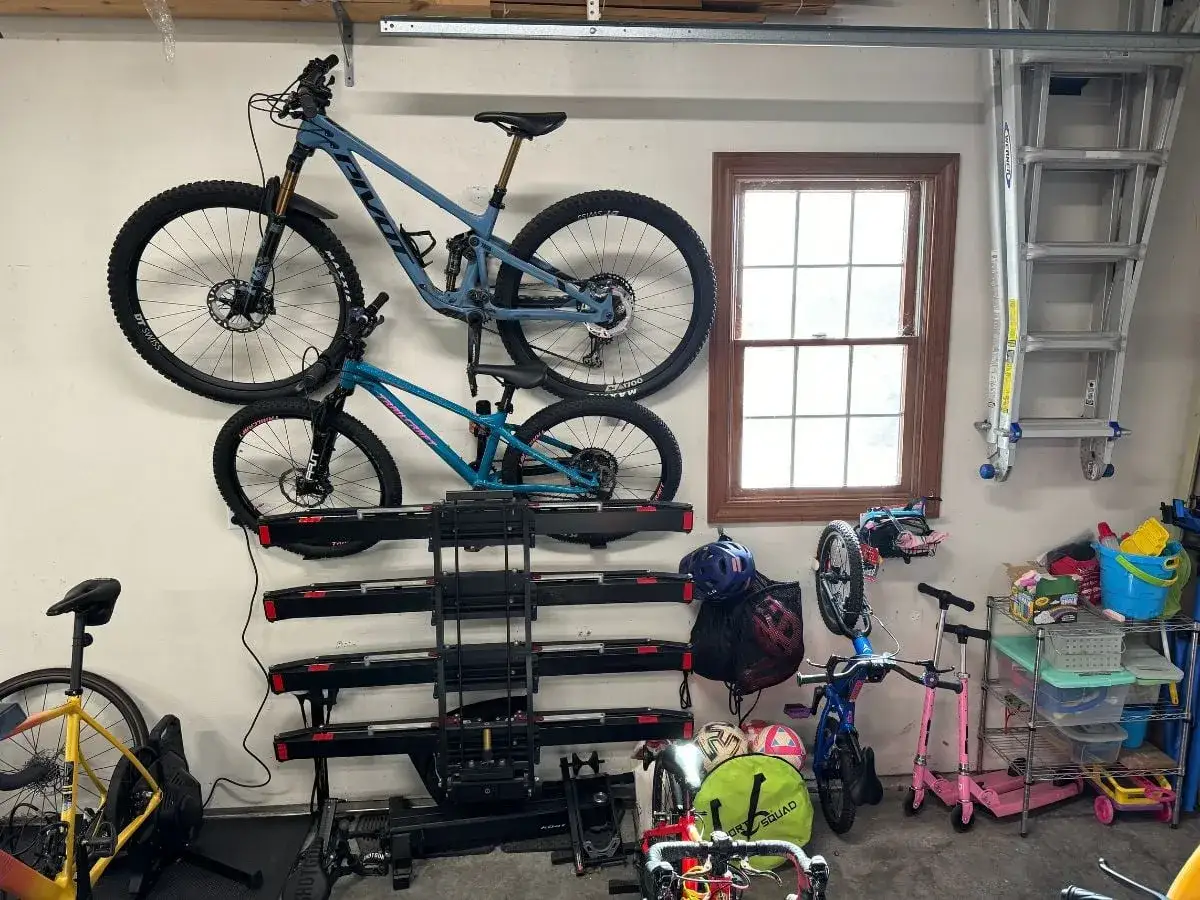 Twee mountainbikes hangen aan de muur, netjes opgeborgen met een mtb ophangen muur systeem. Ook een ladder en opbergrek zijn zichtbaar.