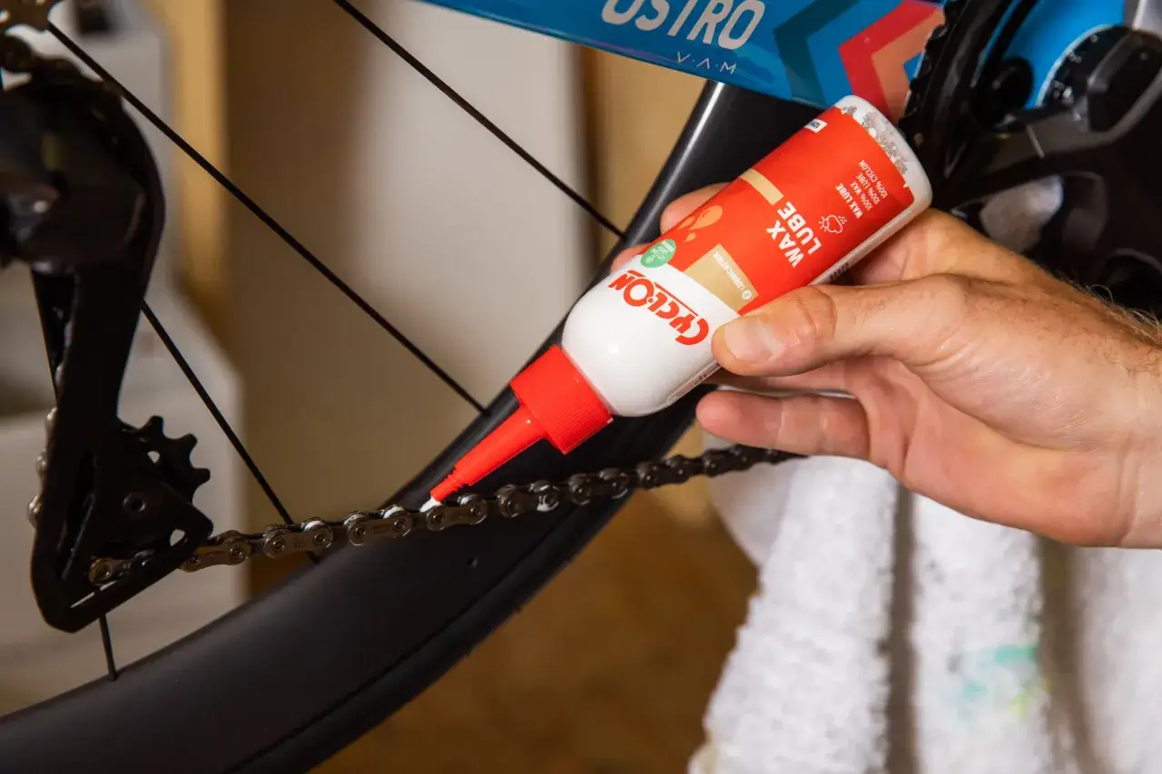 Hand brengt wax lube aan op fietsketting. Zo voorkom je dat de fiets trapt zwaar.