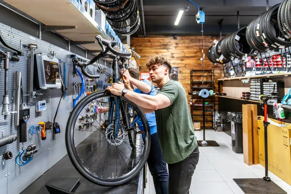 Twee mannen werken aan een fiets in een werkplaats. Ze zijn bezig met het balhoofd fiets afstellen, met gereedschap aan de muur.