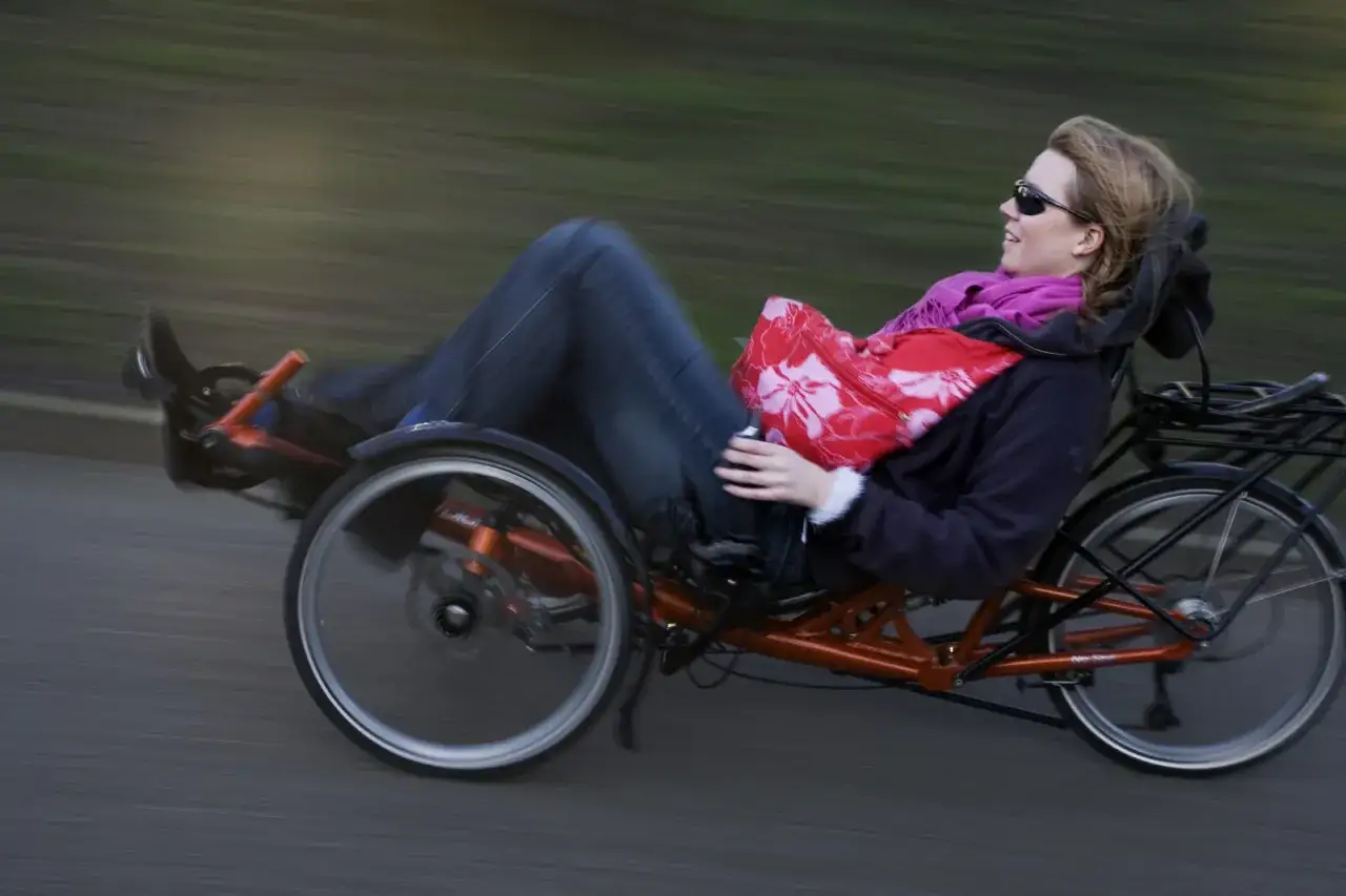 Vrouw op ligfiets, genietend van de wind, met een elektrische fiets die opdrijft tot 30 km/h.