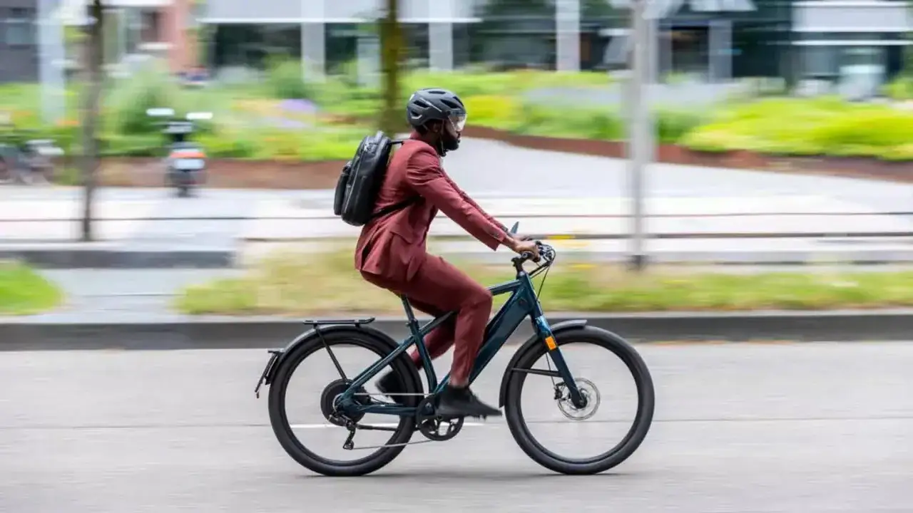 Man in pak op elektrische fiets, met rugzak. Vraag: hoeveel watt mag een elektrische fiets hebben?