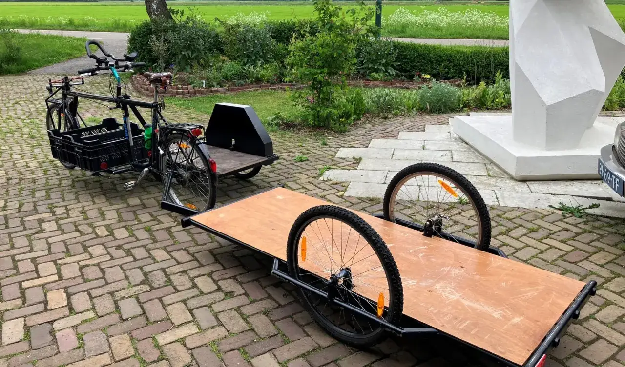 Een fiets met een aanhanger, klaar om een zijspan fiets te maken. De fiets heeft kratten voorop en de aanhanger is een platte bak met twee wielen.