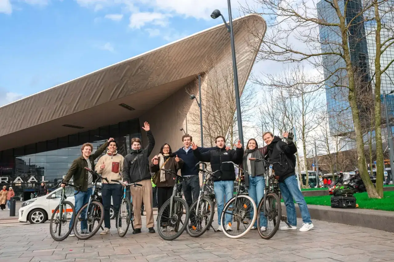 Groep vrienden met fietsen voor een modern gebouw. Ze lachen en zwaaien, blij dat hun swap fiets niet gestolen is.