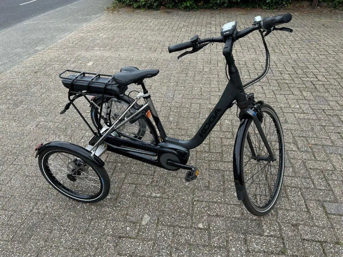 Zwarte Koga fiets omgebouwd naar een stabiele driewieler met bagagedrager en accu.
