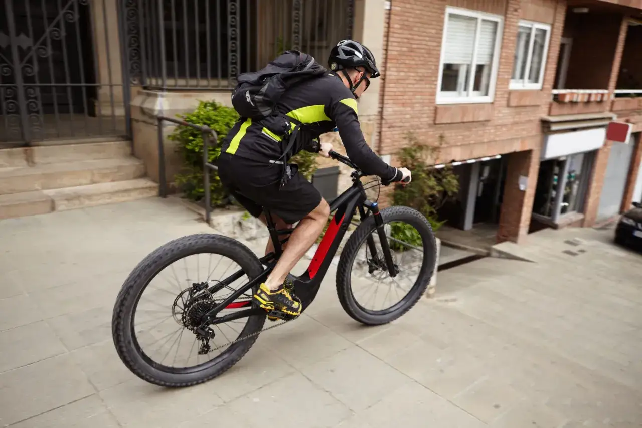 Man op een elektrische fiets, een modern voertuig, fietst een straat af met een rugzak op.