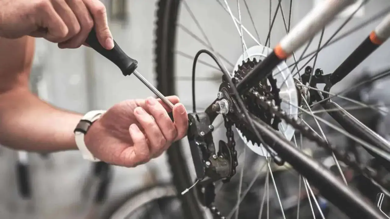 Hand met schroevendraaier stelt derailleur af, lost pinion problemen op. Fietsreparatie in detail.
