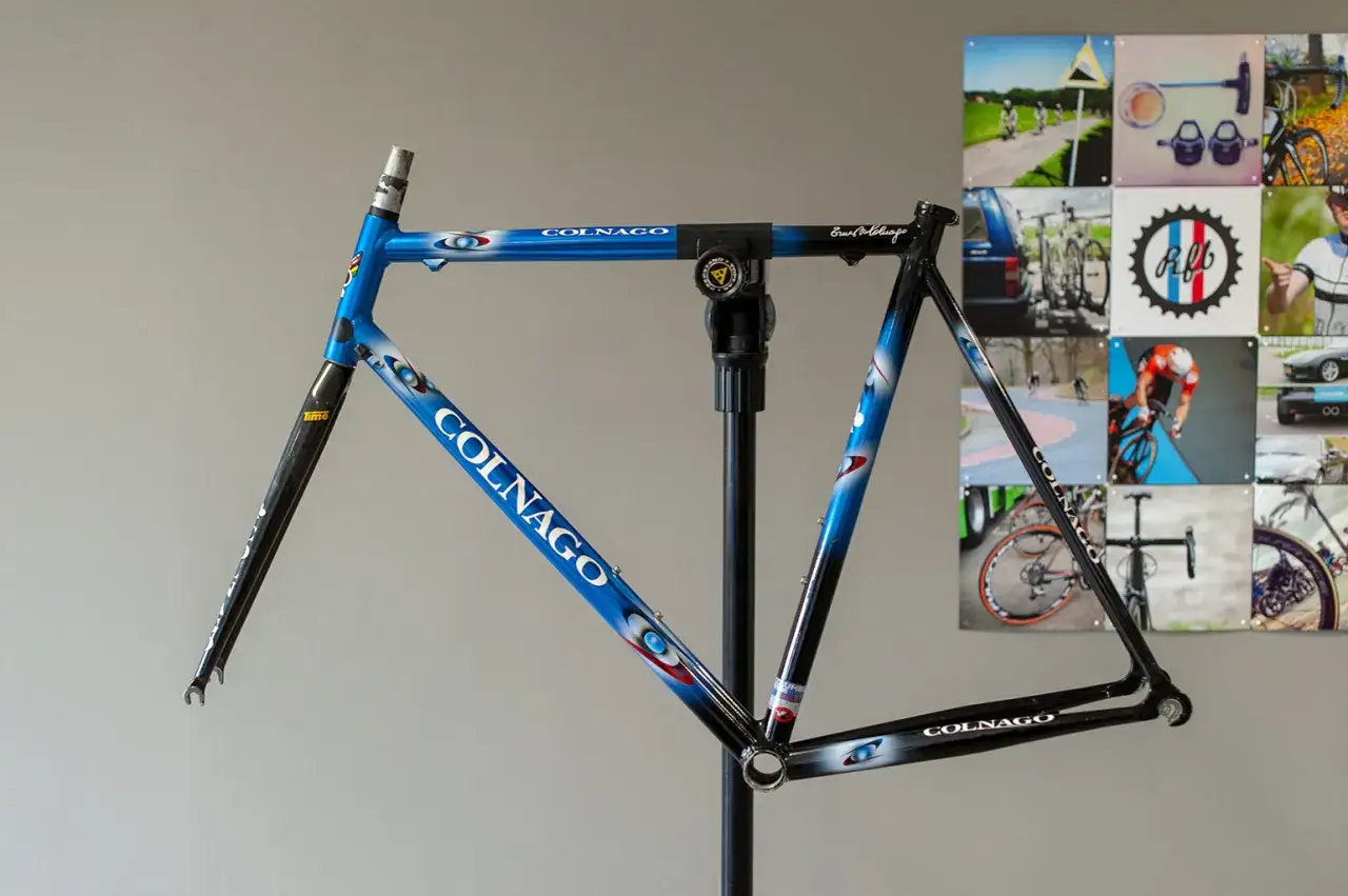 Blauw met witte en rode accenten, een Colnago racefiets frame op een standaard, klaar voor de afmontage.