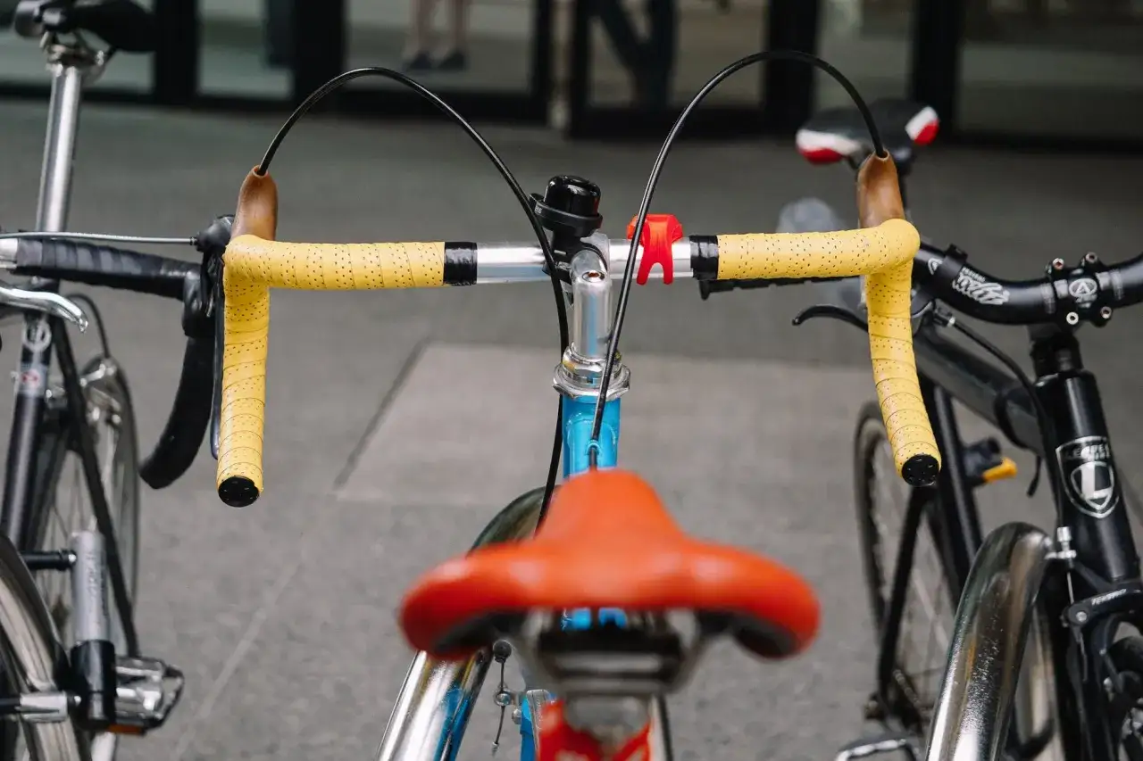 Een klassieke racefiets met felgele stuurlinten en een oranje zadel.
