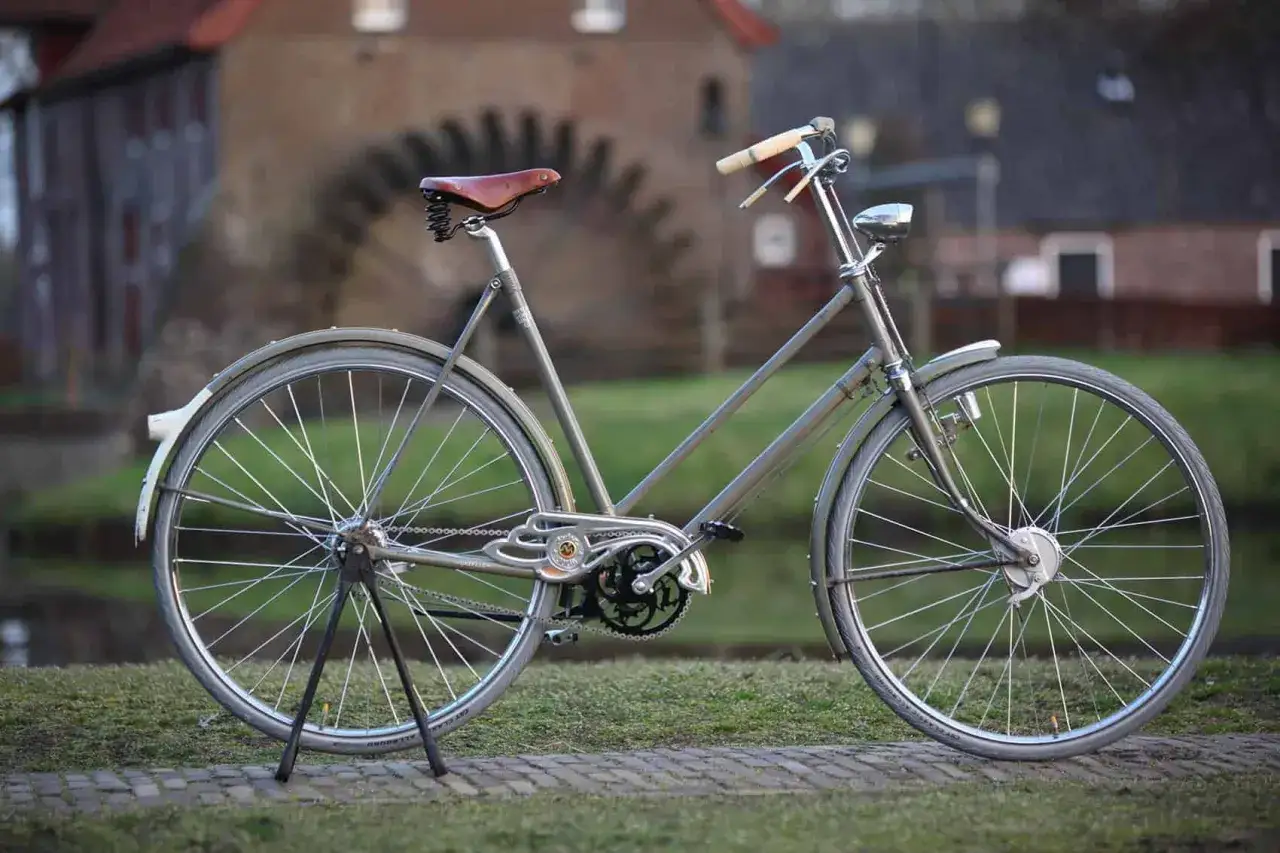 Een klassieke stadsfiets kopen? Deze grijze damesfiets met bruin zadel en houten handvatten staat klaar voor een ritje langs de molen.