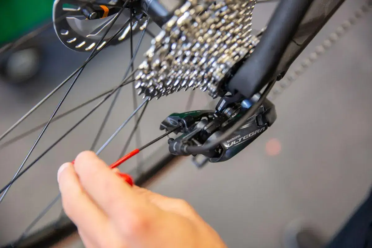 Hand probeert derailleur afstellen lukt niet, met rode inbussleutel aan de Shimano Ultegra derailleur.