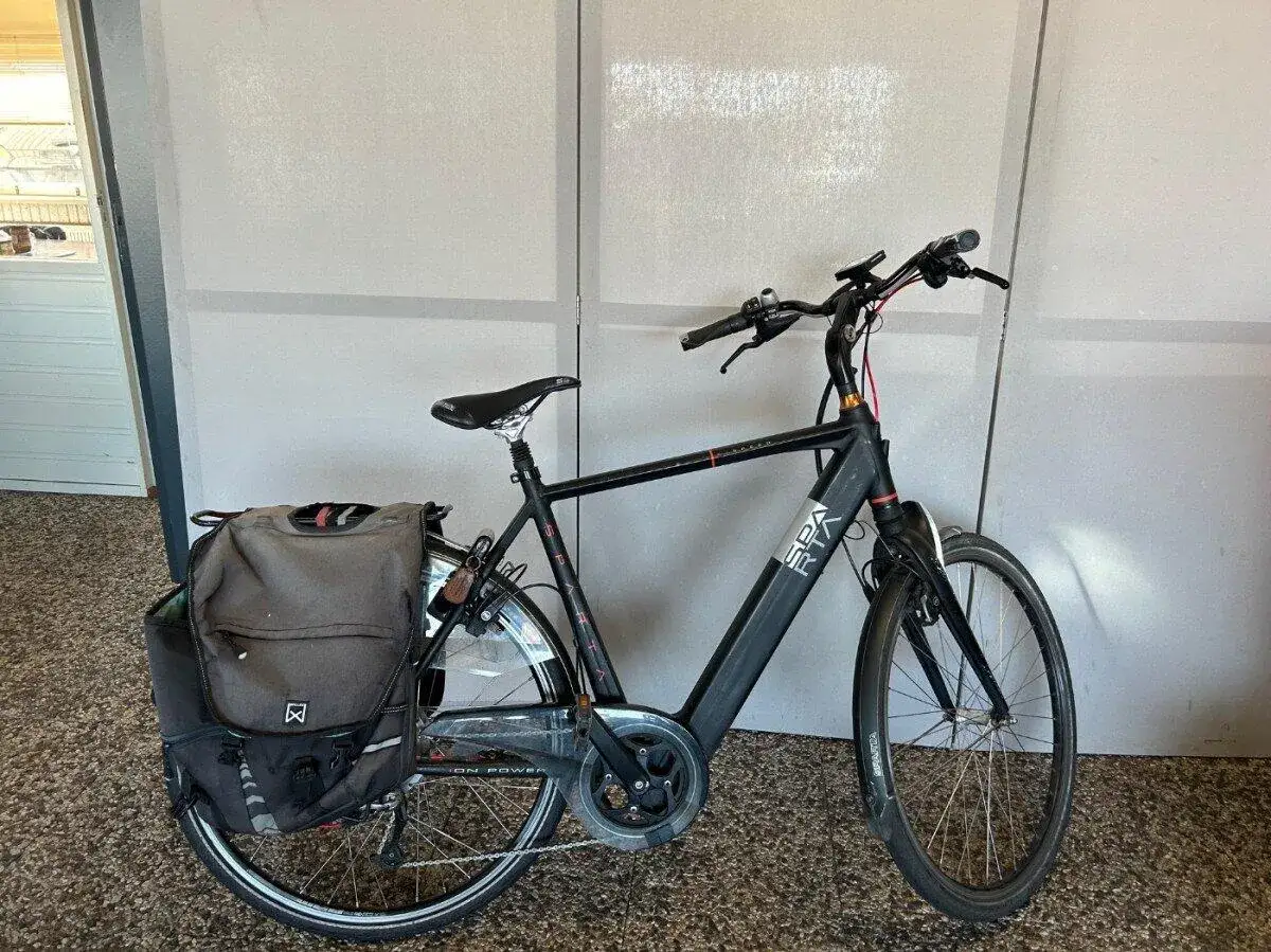 Zwarte Sparta Ion E-Speed e-bike met dubbele fietstassen, klaar voor een rit.
