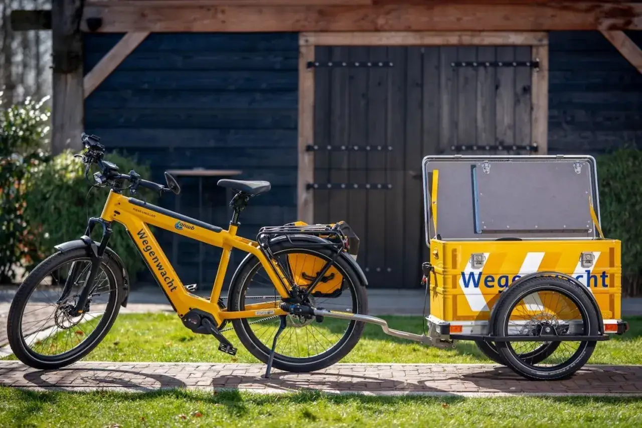 Gele elektrische fiets met aanhanger van de Wegenwacht. Deze fiets mag je aanhangen om spullen te vervoeren.