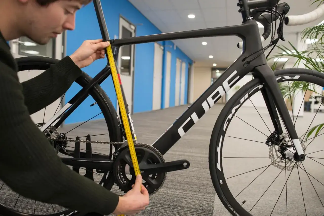 Man meet de cube framemaat met een gele meetlint. De fiets is zwart met witte letters.