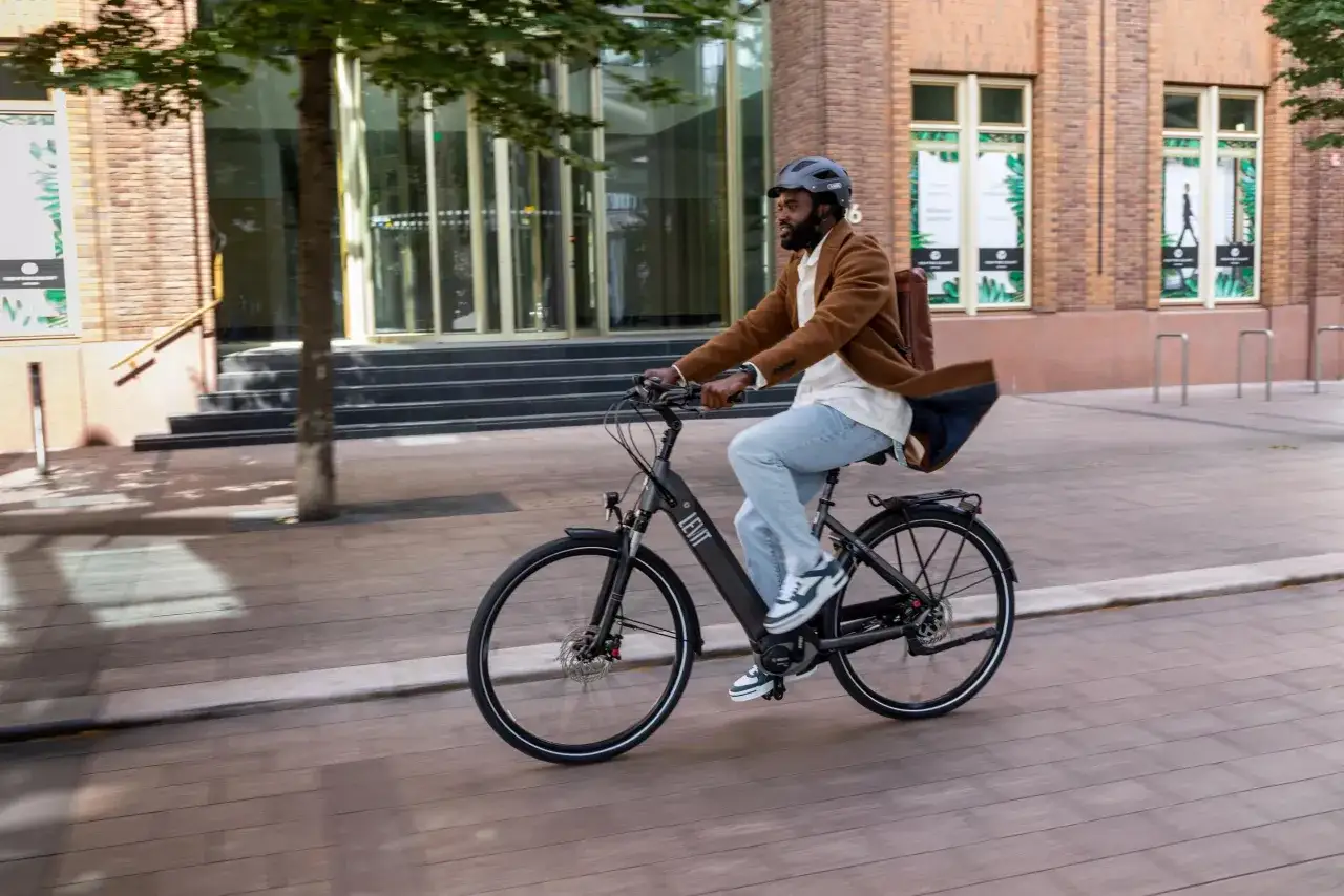Man op elektrische fiets met tas op bagagedrager. De tas lijkt niet zwaar, dus waarschijnlijk niet veel kilo op bagagedrager elektrische fiets.