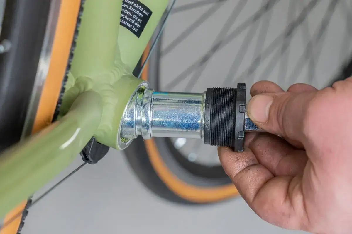 Hand replaces a bicycle's bottom bracket. A new part is being screwed into the green frame.