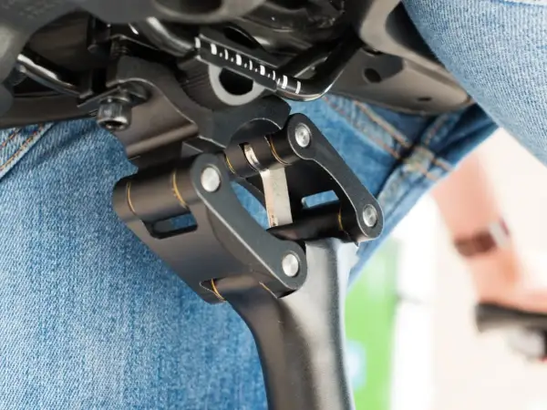 Gedetailleerde close-up van een fietszadel met een verende zadelpen afstellen. De mechanische delen zijn duidelijk zichtbaar, met een persoon in spijkerbroek op de achtergrond.