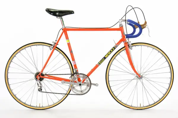 Klassieke racefiets in fel oranje, met "Eddy Merckx" op de buis. Een iconisch stukje fietsgeschiedenis.