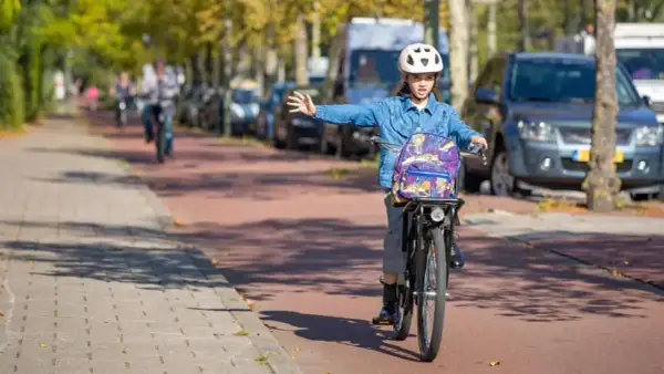Meisje op fiets met rugzak en helm geeft richting aan, een voorbeeld van verkeersregels voor fietsers.