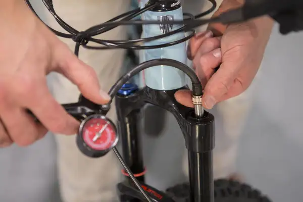 Iemand stelt de verende voorvork van een e-bike af met een pomp en manometer.