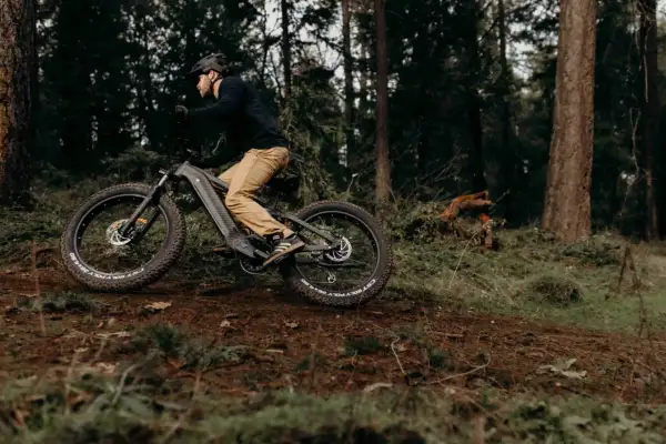 Man op een elektrische fiets in het bos, de fiets trapt zwaar door het ruige terrein.