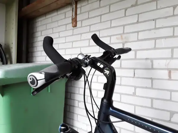 Stuur van een fiets met handvatten en een bel. Geen mountainbike bar ends te zien, wel een groene bak ernaast.