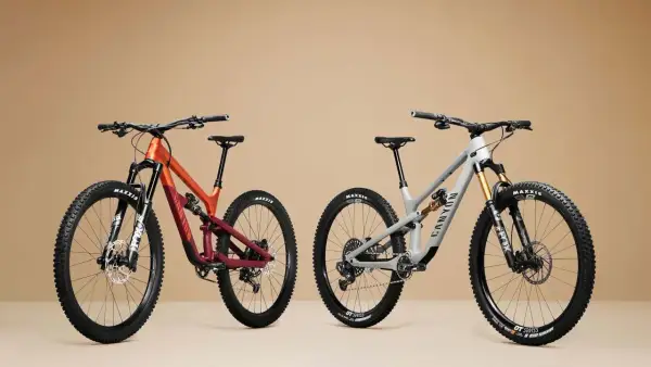 Twee mountainbikes, één oranje/rood en één grijs, met duidelijke wielmaat en Maxxis banden.
