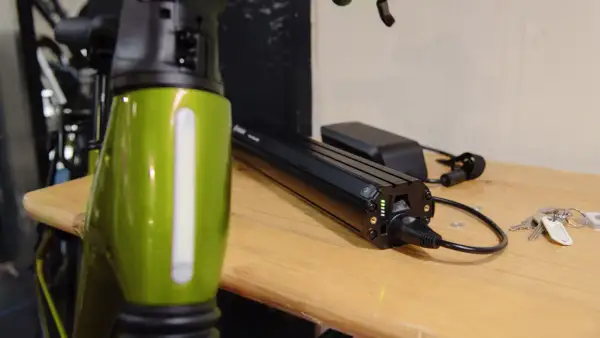 Een groene e-bike frame staat naast een Bosch accu die aan het opladen is. De accu heeft groene lampjes die de laadstatus aangeven.