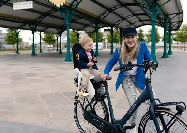 Een hippe mamafiets met een lachend kindje in de kinderzitje, klaar voor een ritje onder een stationskap.