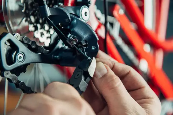 Hand knipt versnellingskabel fiets. De derailleur en ketting zijn zichtbaar, met een rode fietsframe op de achtergrond.