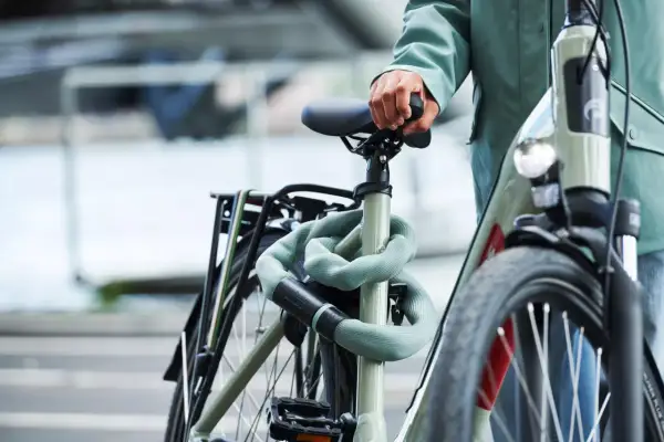 Een persoon met een groene jas houdt het zadel van een fiets vast. De fiets is beveiligd met een lichtgroene kettingslot. Denk aan een gps tracker fiets inbouwen voor extra veiligheid.