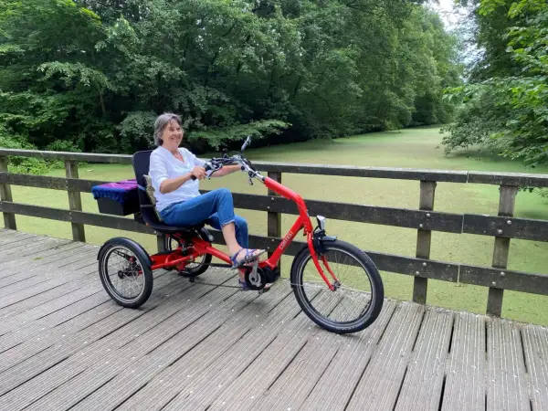 Vrolijke vrouw geniet op een driewieler, een veilige fiets voor ouderen, langs een groen kanaal.