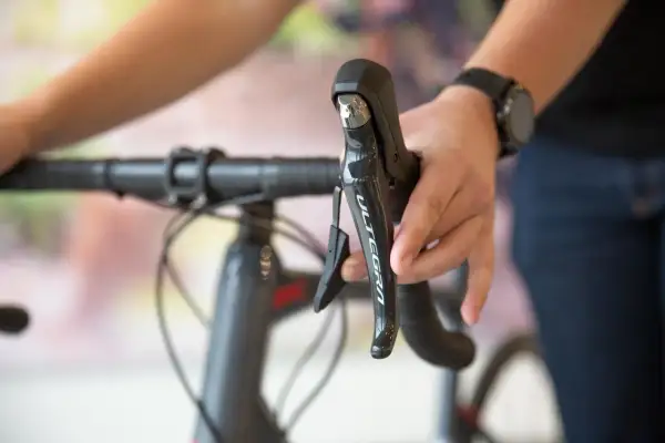 Hand op het schakelen van een racefiets, met de Ultegra-aanduiding zichtbaar op de remhendel.