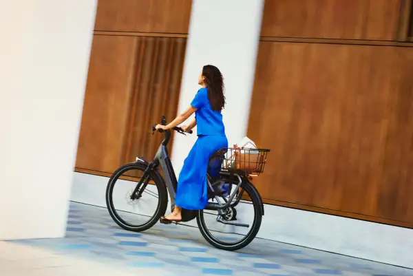 Vrouw in blauwe jurk geniet van een ritje op haar nieuwe fiets, met boodschappen in de mand. Een perfecte fiets kiezen is een feest!