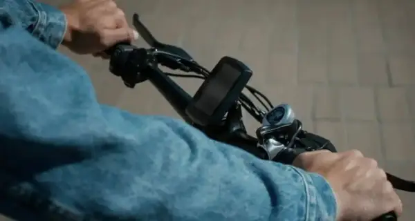 Handen aan het stuur van een elektrische fiets, klaar voor een rit. De aansluiting van de accu is niet zichtbaar, maar de fiets is klaar voor gebruik.