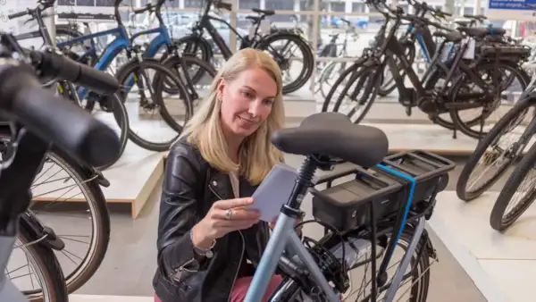 Vrouw overweegt wel of geen elektrische fiets in een fietsenwinkel, omringd door diverse modellen.