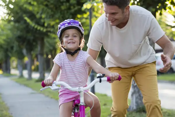 Een vader leert zijn dochter fietsen, met een helm op voor haar veiligheid. Zo zorgen we ervoor dat elk kind veilig op de fiets zit.