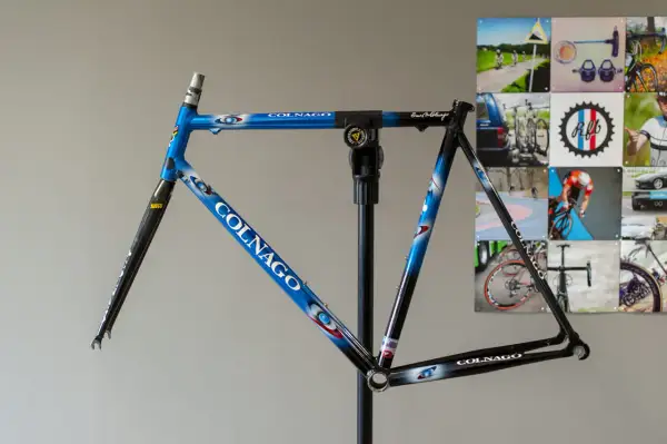 Blauw met witte en rode accenten, een Colnago racefiets frame op een standaard, klaar voor de afmontage.