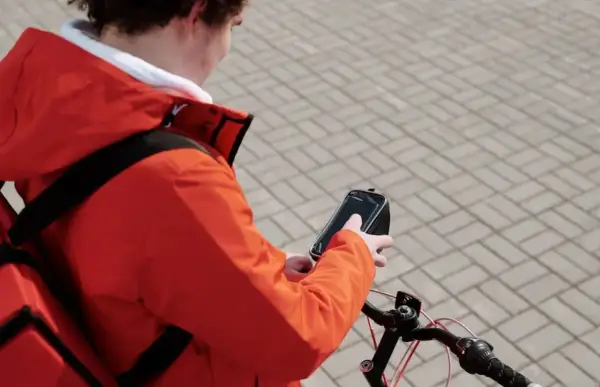 Bezorgbezorger in oranje jas checkt zijn telefoon op de fiets, hopelijk geen boete telefoon fiets!