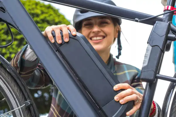 Vrolijke vrouw met helm bevestigt de accu van haar e-bike. Goed accu onderhoud zorgt voor zorgeloze fietstochten.